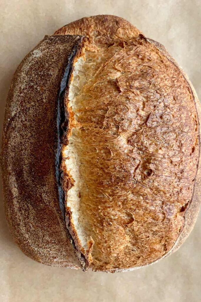 A freshly baked sourdough loaf resting on baking paper.