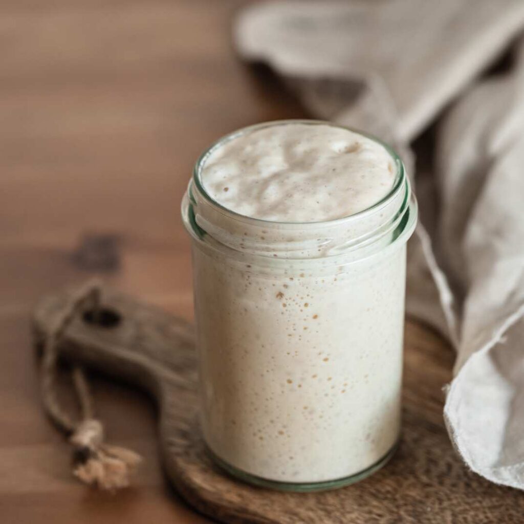 wheat sourdough starter in a glass jar on a wooden cutting board